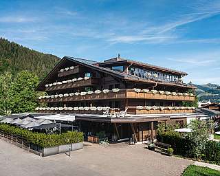 Holzhotel mit vielen pinken Blumen auf Balkonen und Sonnenschirmen im Außenbereich