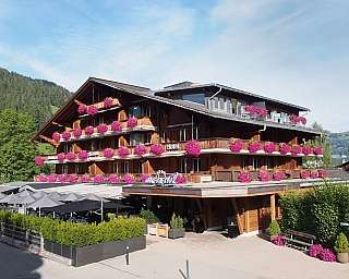 Holzhotel mit vielen pinken Blumen auf Balkonen und Sonnenschirmen im Außenbereich