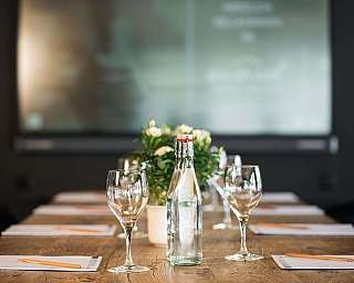 Une table de conférence avec des verres, une bouteille d'eau et des fleurs.