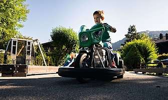 Un garçon roule sur une moto jouet verte à l'extérieur.