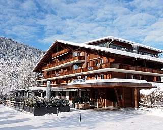 A wooden house in the snow with mountains in the background.