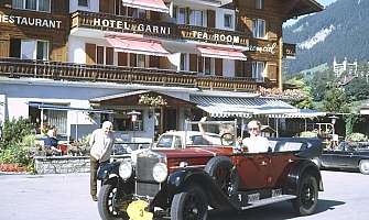 Une voiture ancienne rouge devant un hôtel dans les montagnes.
