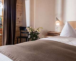 A bright bedroom with a bed, chair, and plants.